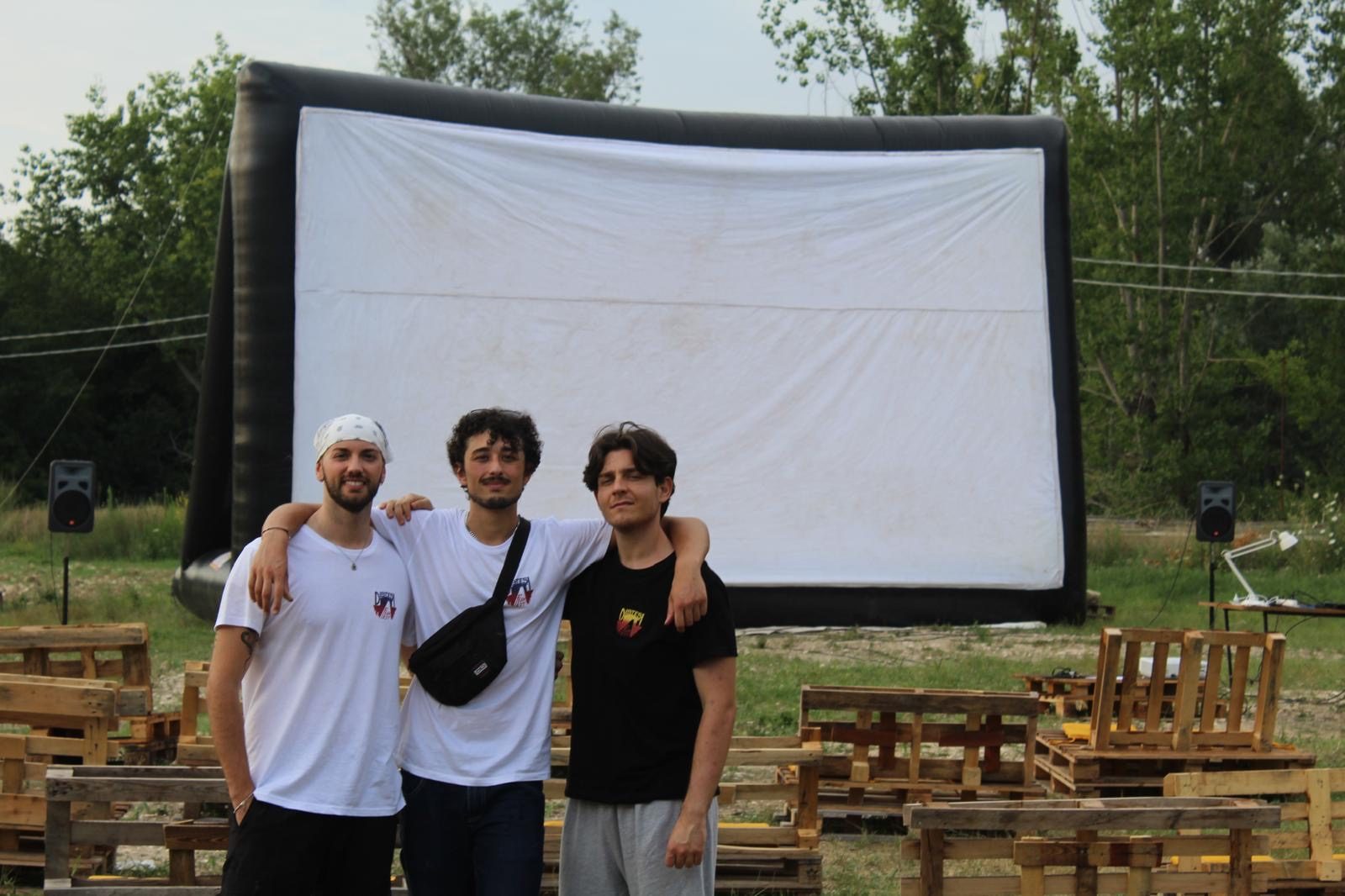 Tre ragazzi dell'associazione davanti allo schermo gonfiabile, tra le panche di bancali