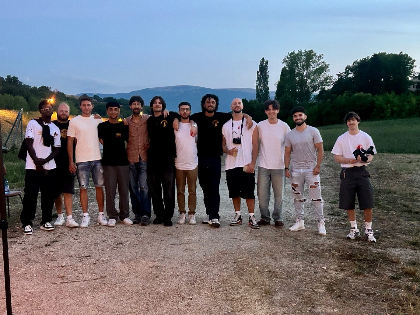 Gruppo di volontari in posa al tramonto su una strada sterrata, con le colline sullo sfondo